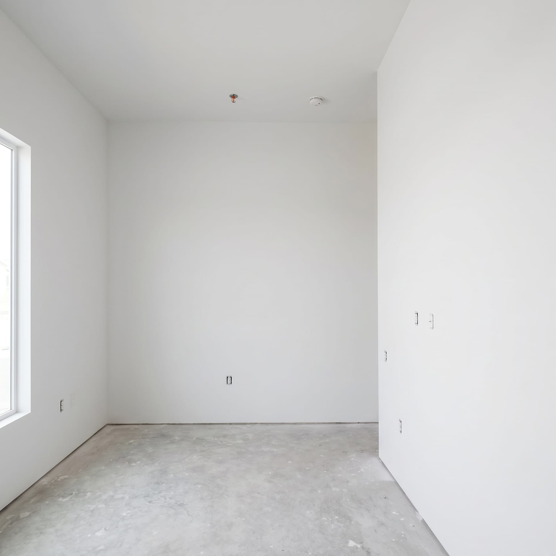 Finished back room with a tall window on the left and concrete floor.